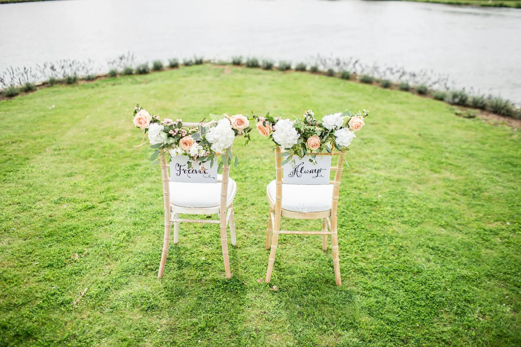 Two ceremony chairs decorated with flowers by the water