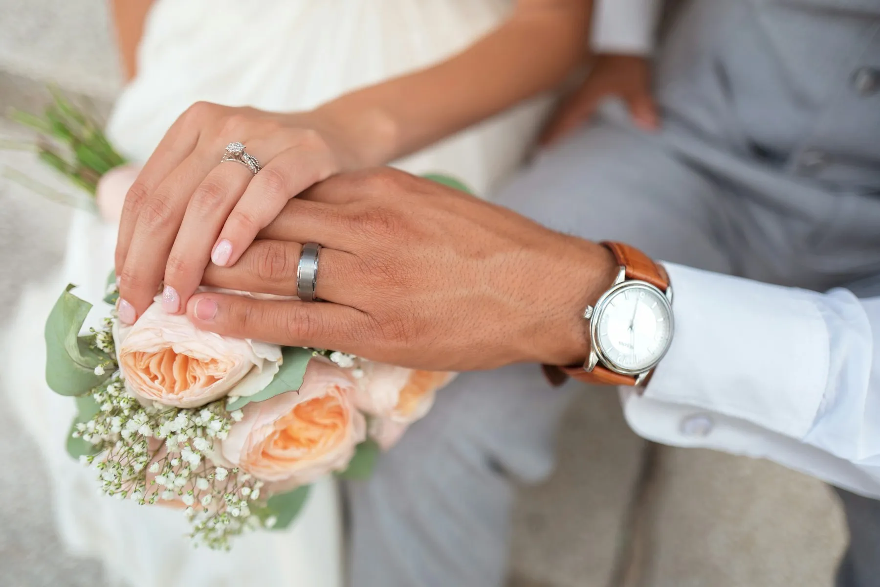 Couple holding hands with wedding rings and a bouquet
